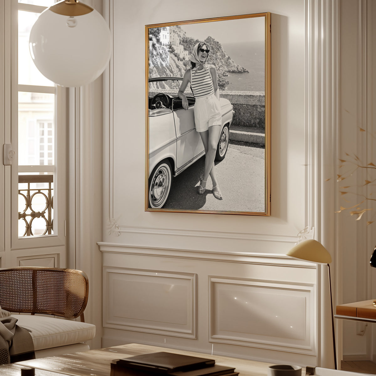 Woman leaning on vintage convertible by the sea print shown in a gold frame in a Parisian paneled living room