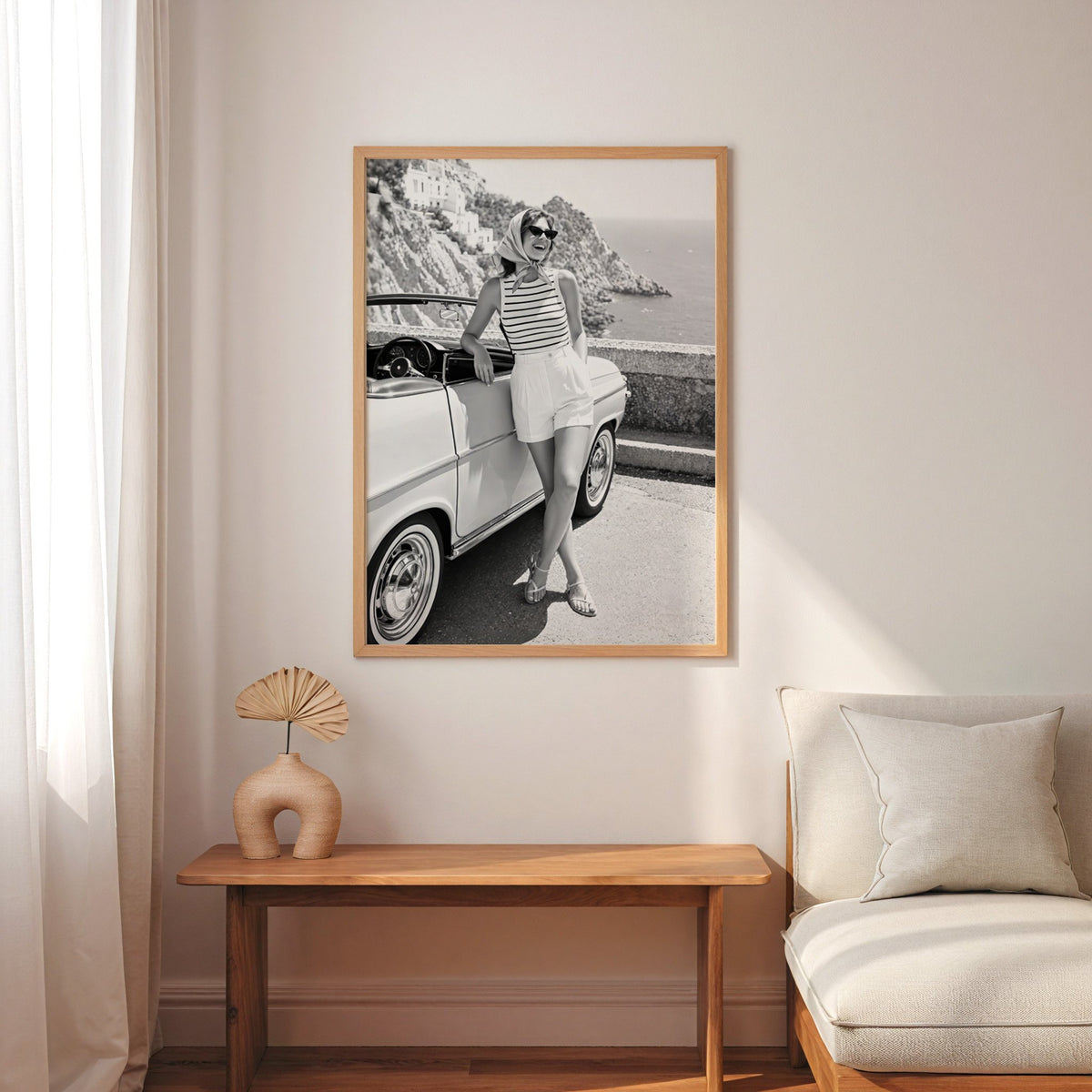 Woman leaning on vintage convertible by the sea print in an oak frame above a narrow console with an arched vase