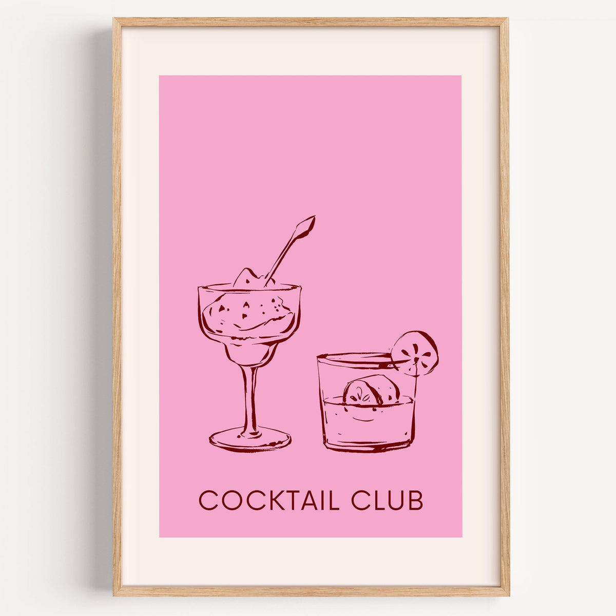 Cocktail Club sketched glasses pink print in a light oak frame on a plain white wall