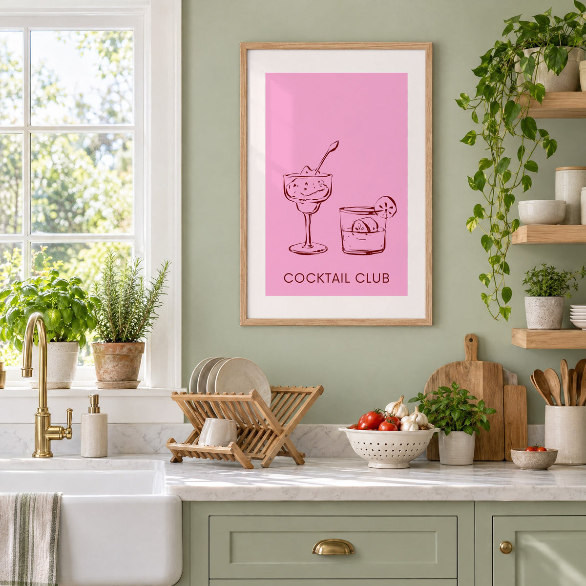 Cocktail Club sketched glasses pink print in an oak frame on a sage green kitchen wall beside a farmhouse sink and herbs