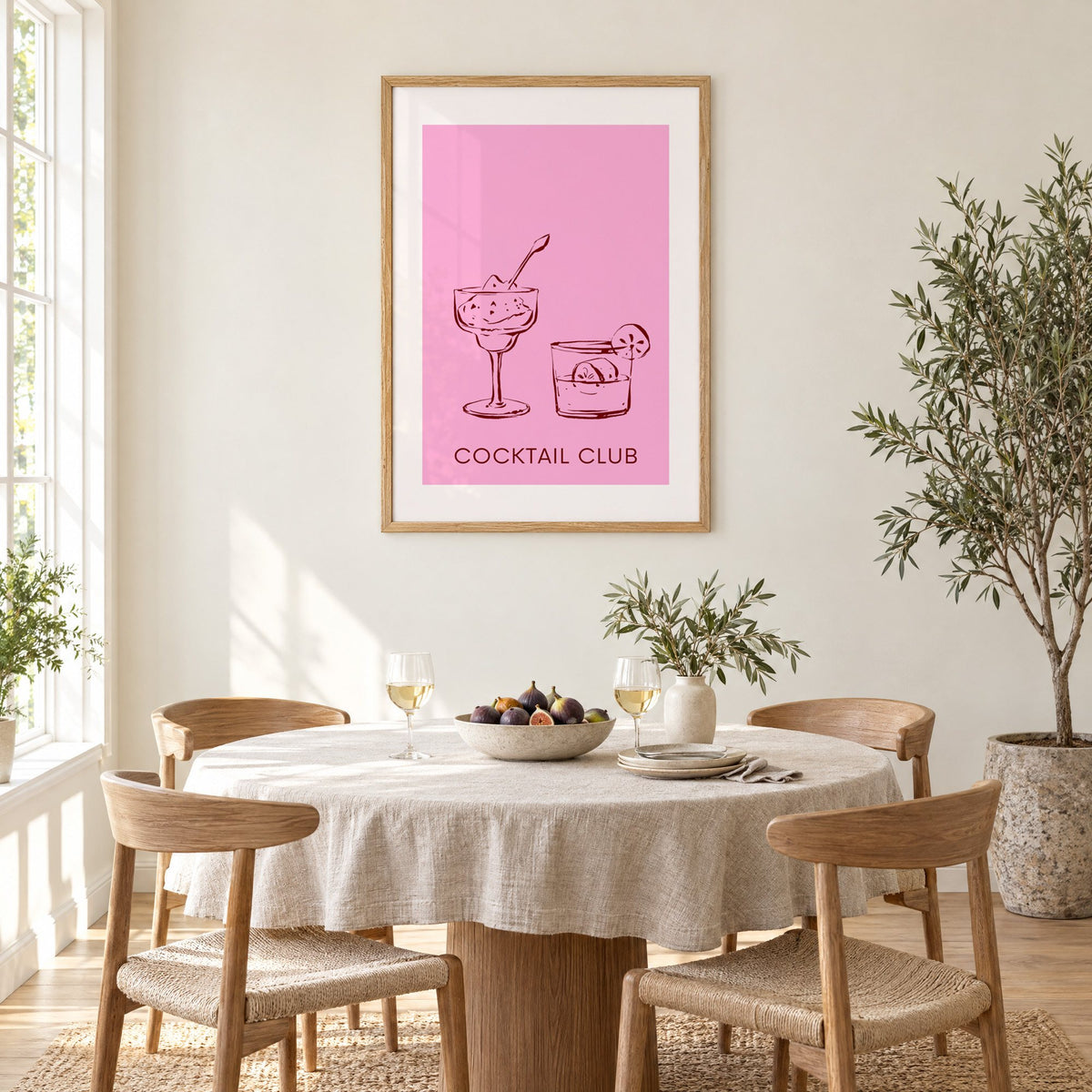 Cocktail Club sketched glasses pink print in an oak frame above a round linen-covered dining table with figs and wine