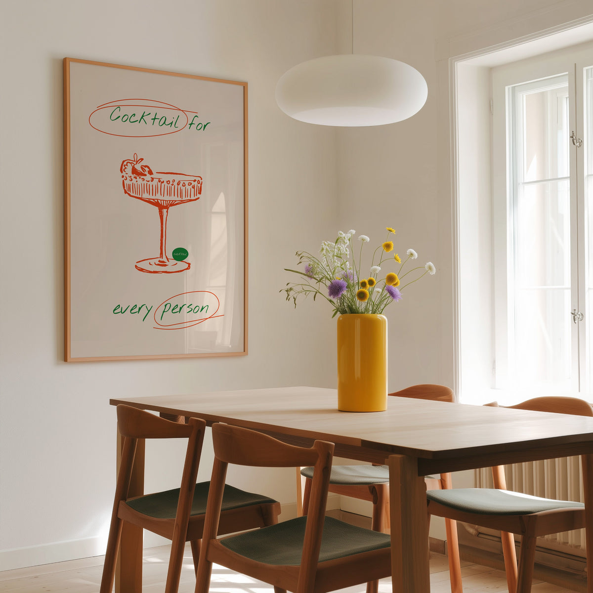 Cocktail coupe print in a slim oak frame above a dining table under a pendant lamp