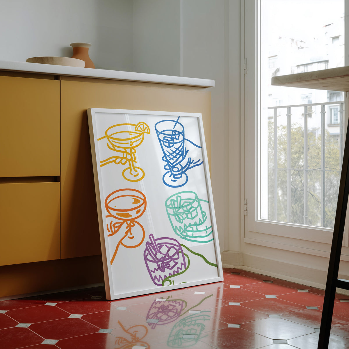 Cocktail glasses print in a white frame against yellow cabinets on a red tiled floor