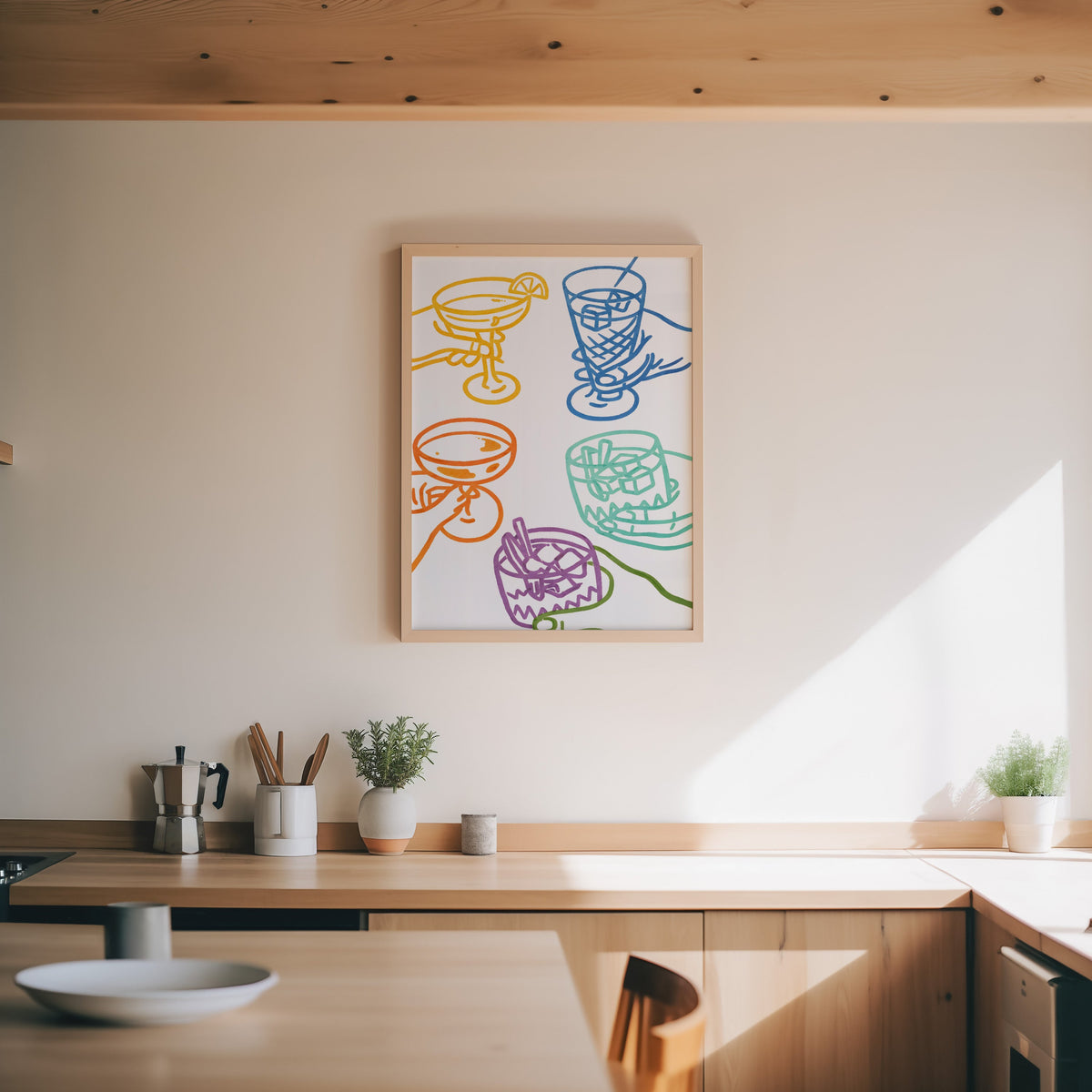 Cocktail glasses print in an oak frame above a wood counter with a moka pot and herbs
