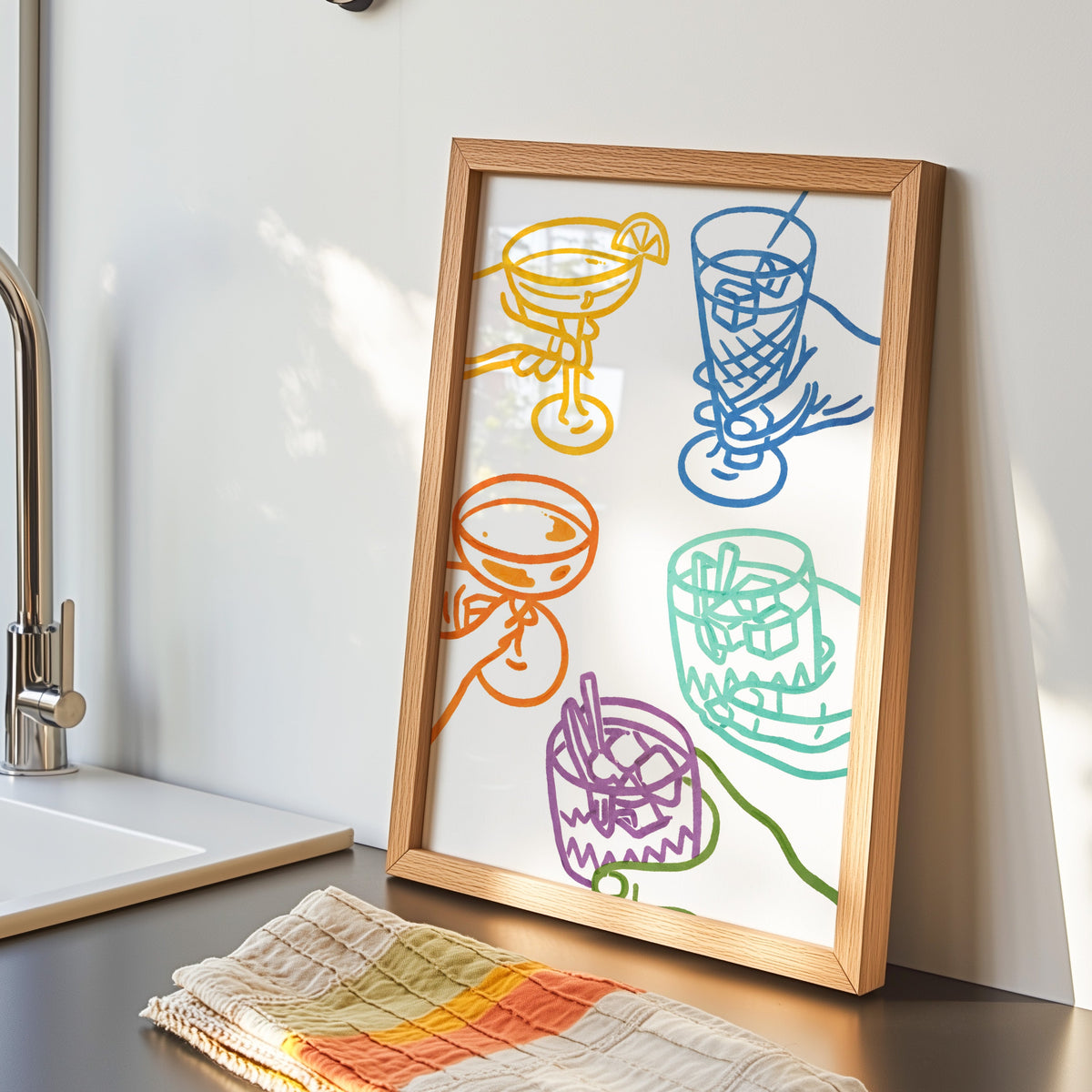 Cocktail glasses print in an oak frame by the kitchen sink beside a striped tea towel