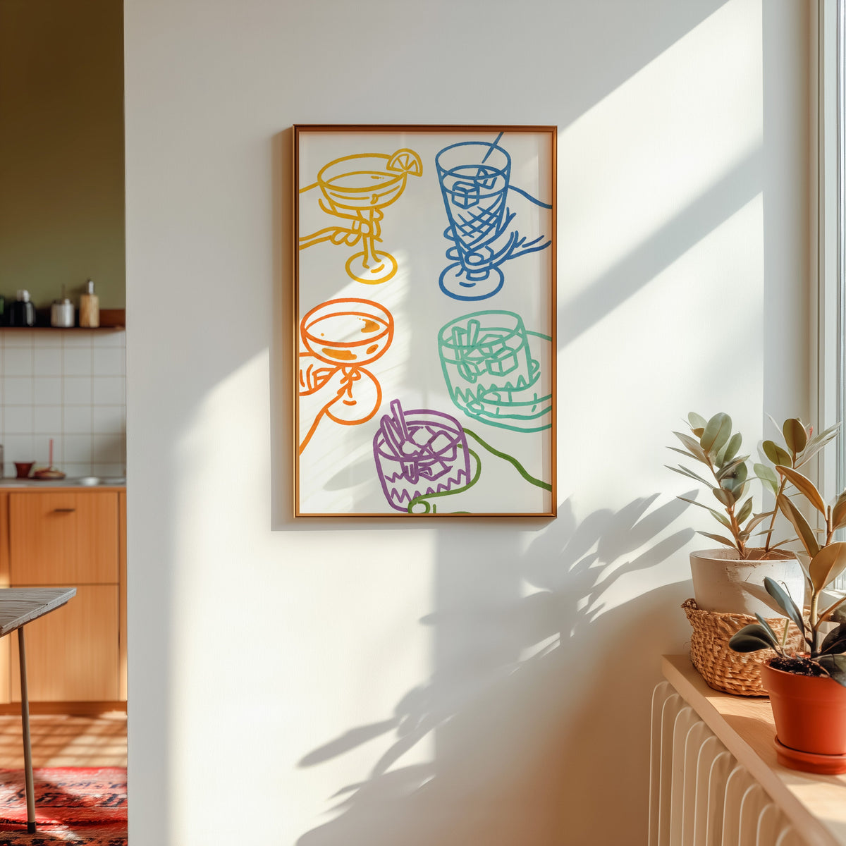 Cocktail glasses print in a gold frame in sunlight with plants on the ledge and a kitchen beyond