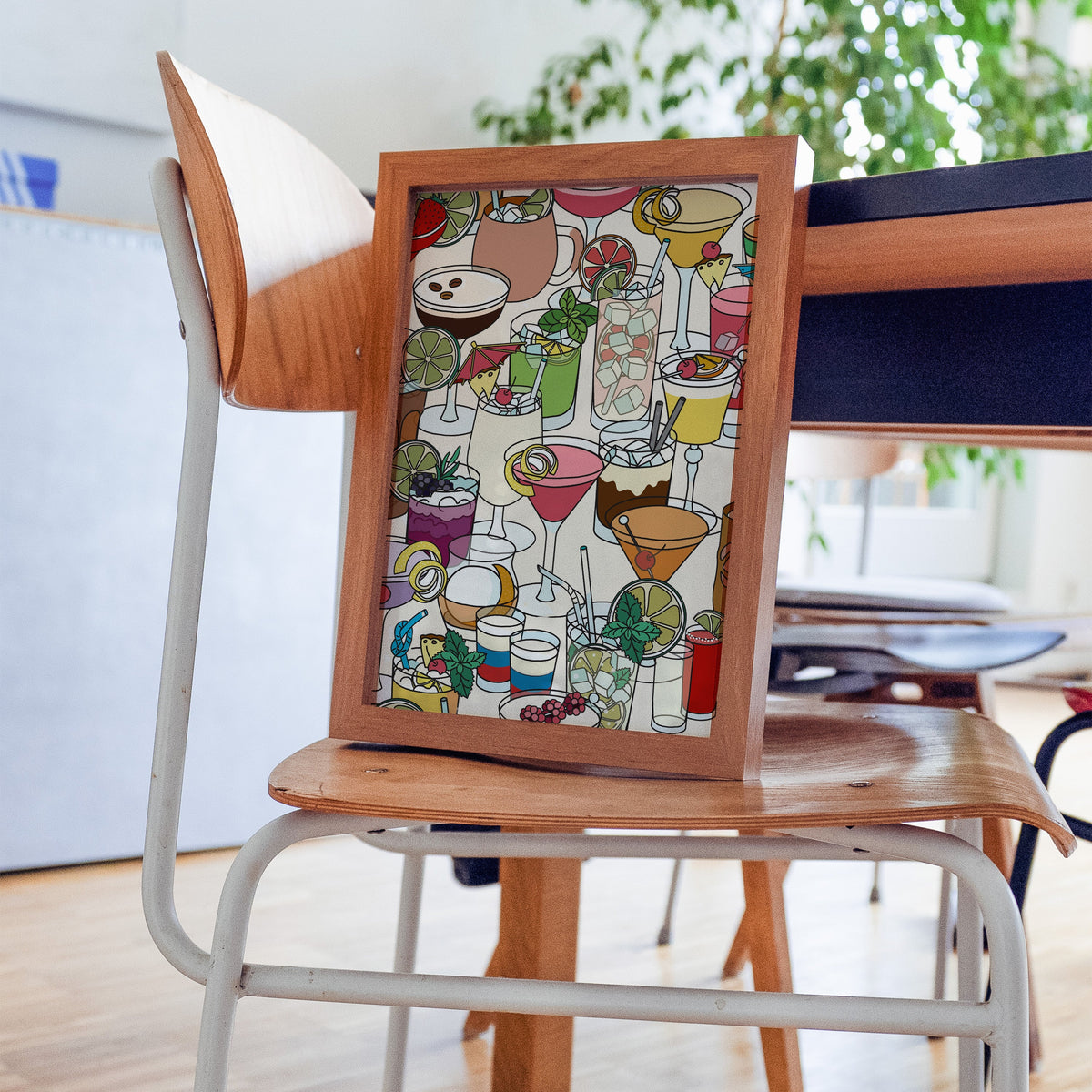 Dense cocktail glasses pattern print in a walnut frame resting on a plywood studio chair beside a dark desk