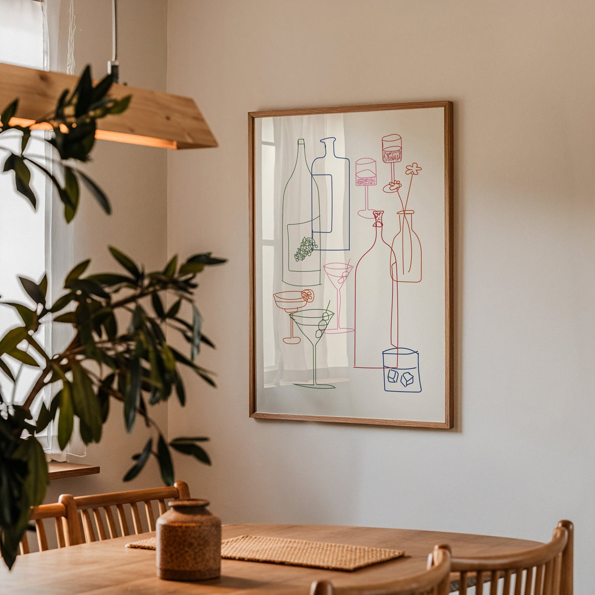 Cocktail glassware line art print in a walnut frame above a dining table beside an olive tree
