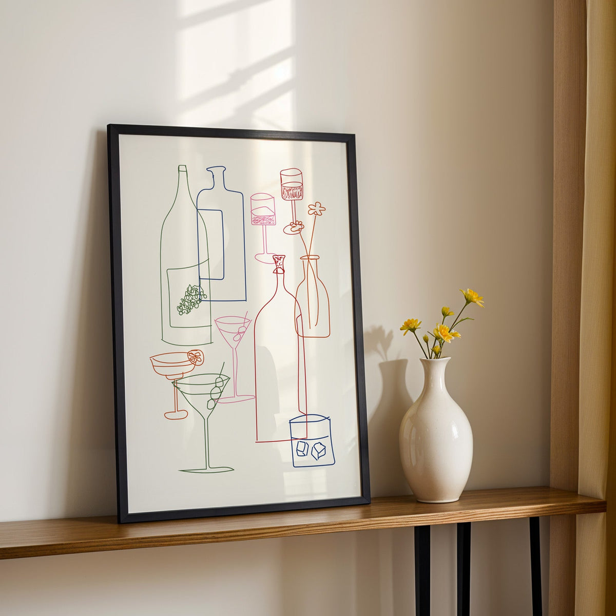 Cocktail glassware line art print in a black frame on a console table with yellow daisies