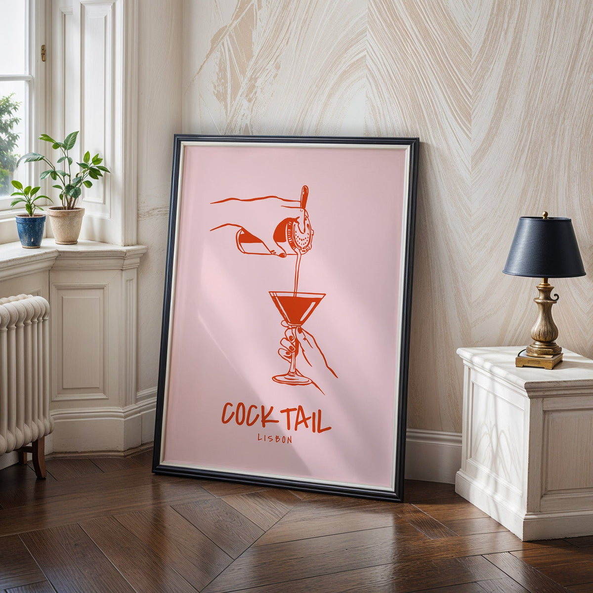 Cocktail Lisbon print in a black frame on a dark herringbone floor beside a radiator