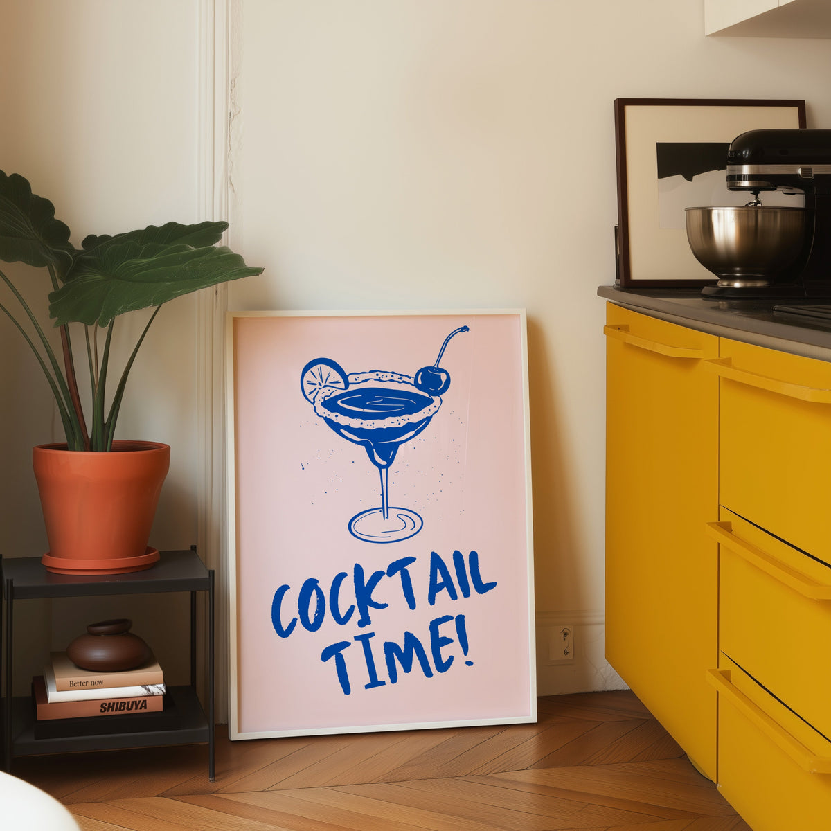 Cocktail Time margarita print in a white frame leaning on parquet beside a bright yellow kitchen