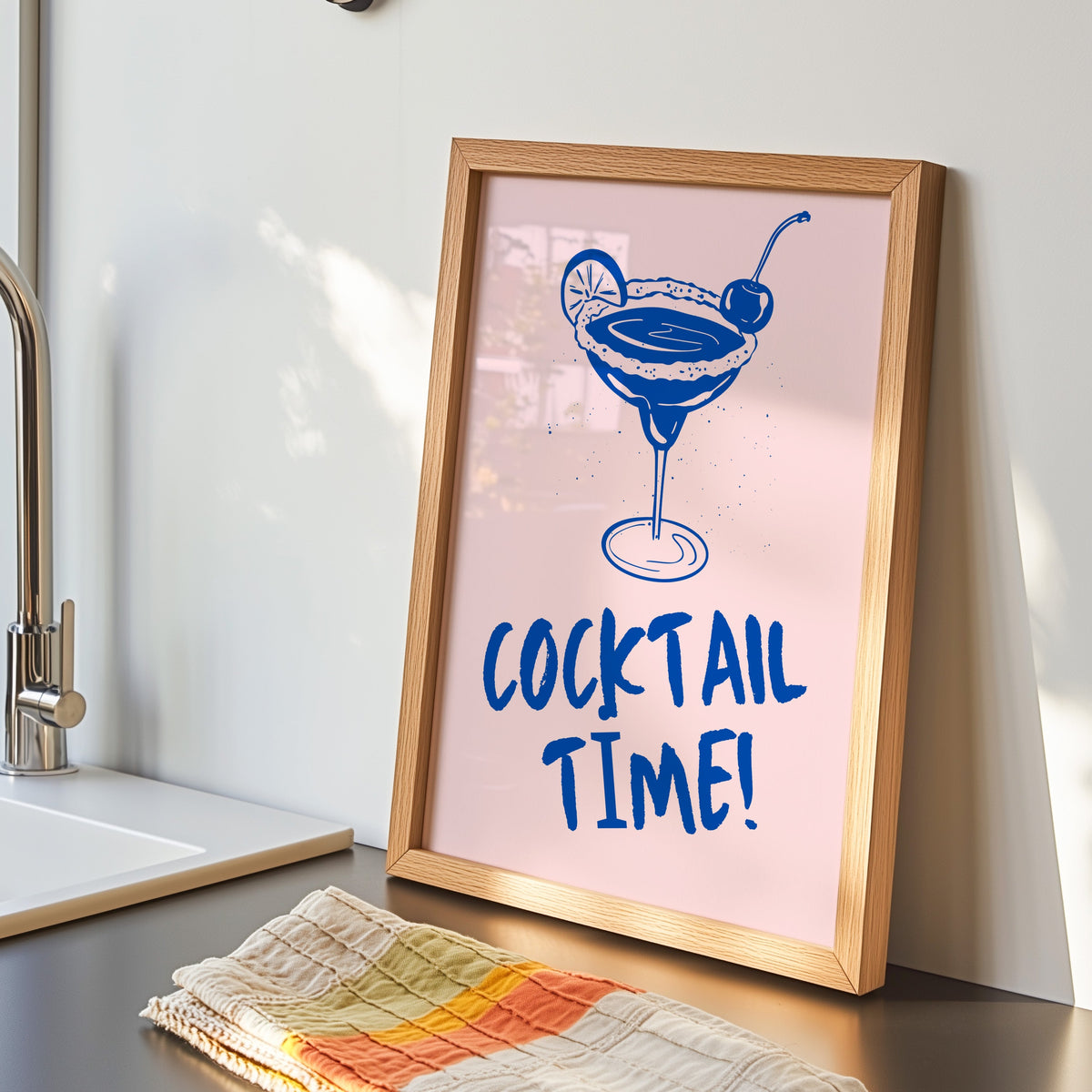 Cocktail Time margarita print in an oak frame by the kitchen sink beside a striped tea towel