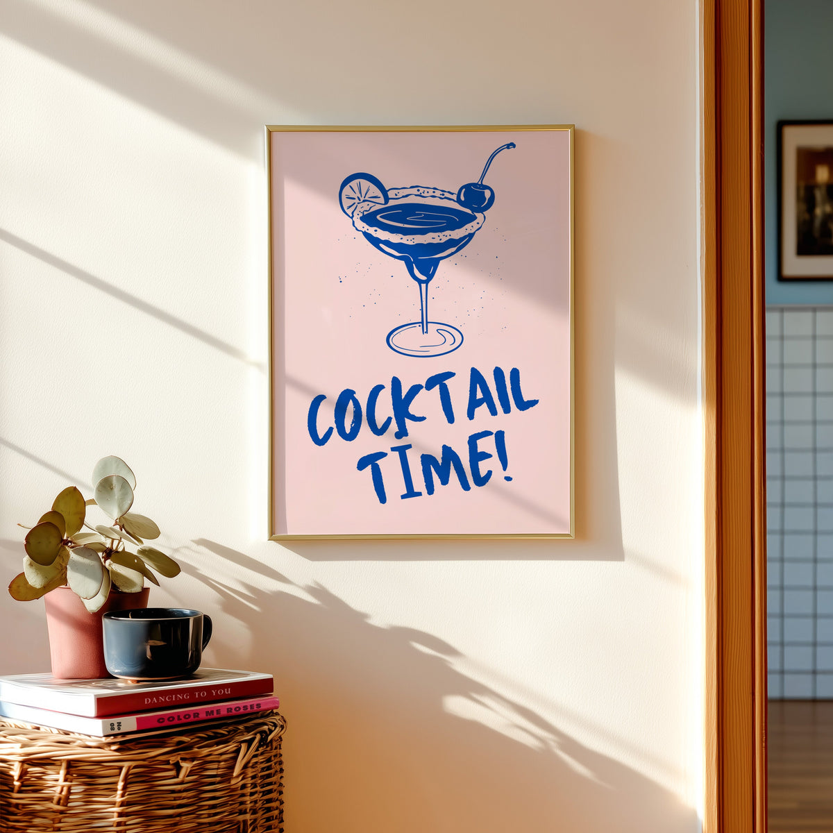 Cocktail Time margarita print shown in a gold frame above a basket of books and a pilea plant