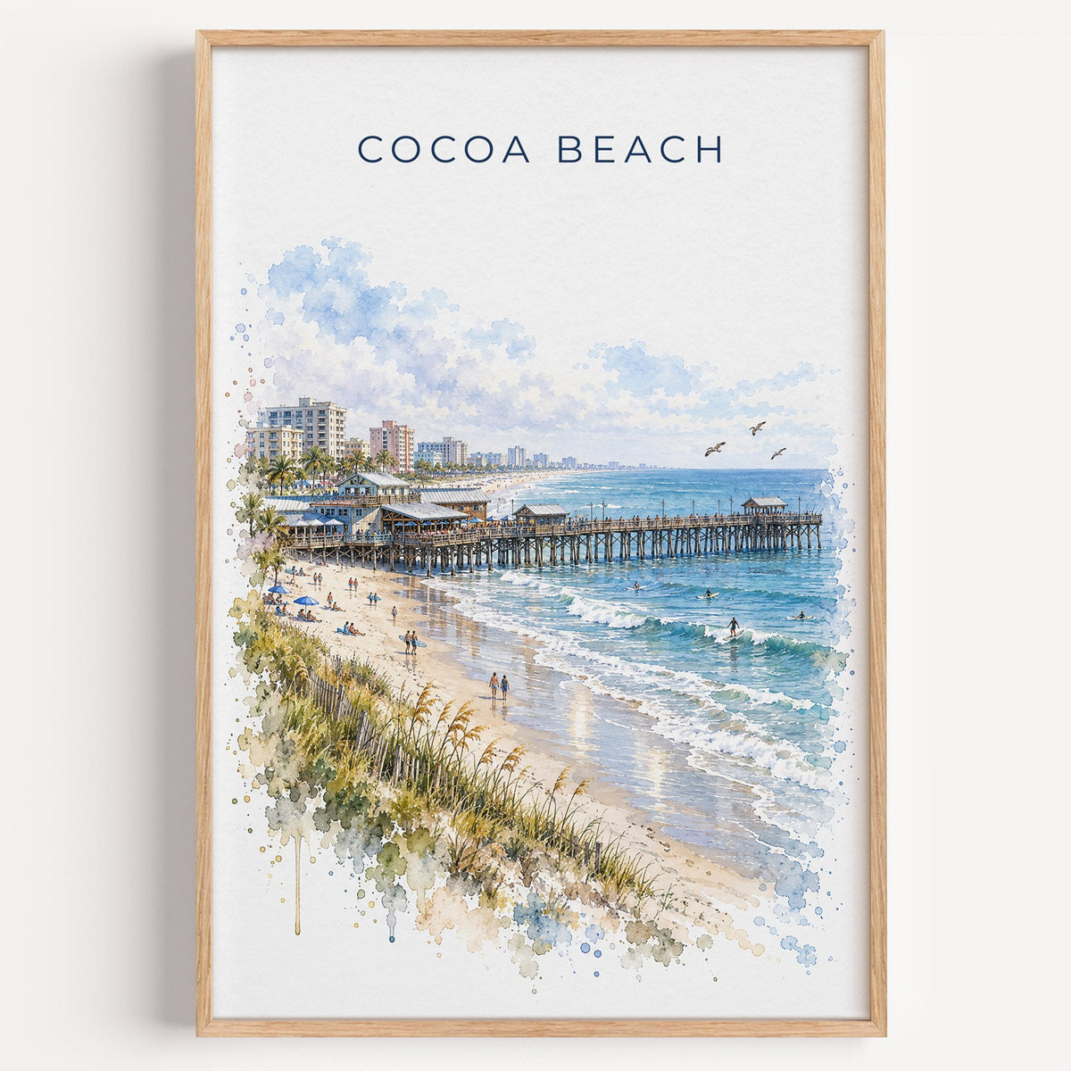 Cocoa Beach watercolor print in a light oak frame on a plain white wall