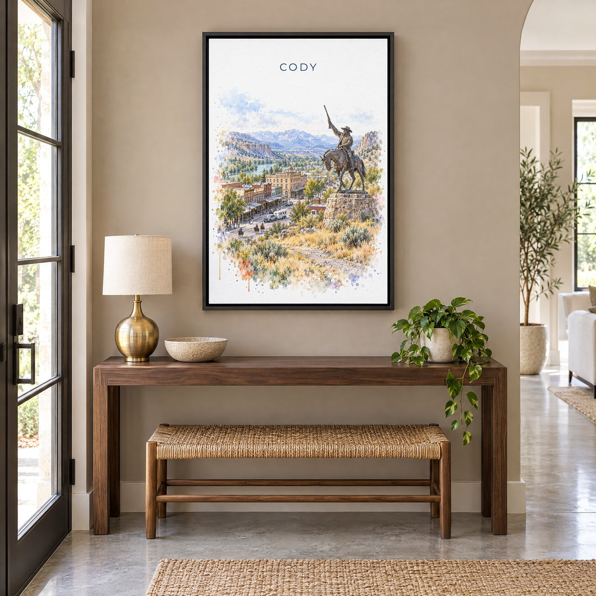 Cody, Wyoming watercolor print as a black floater canvas above a walnut console and woven bench in an entryway