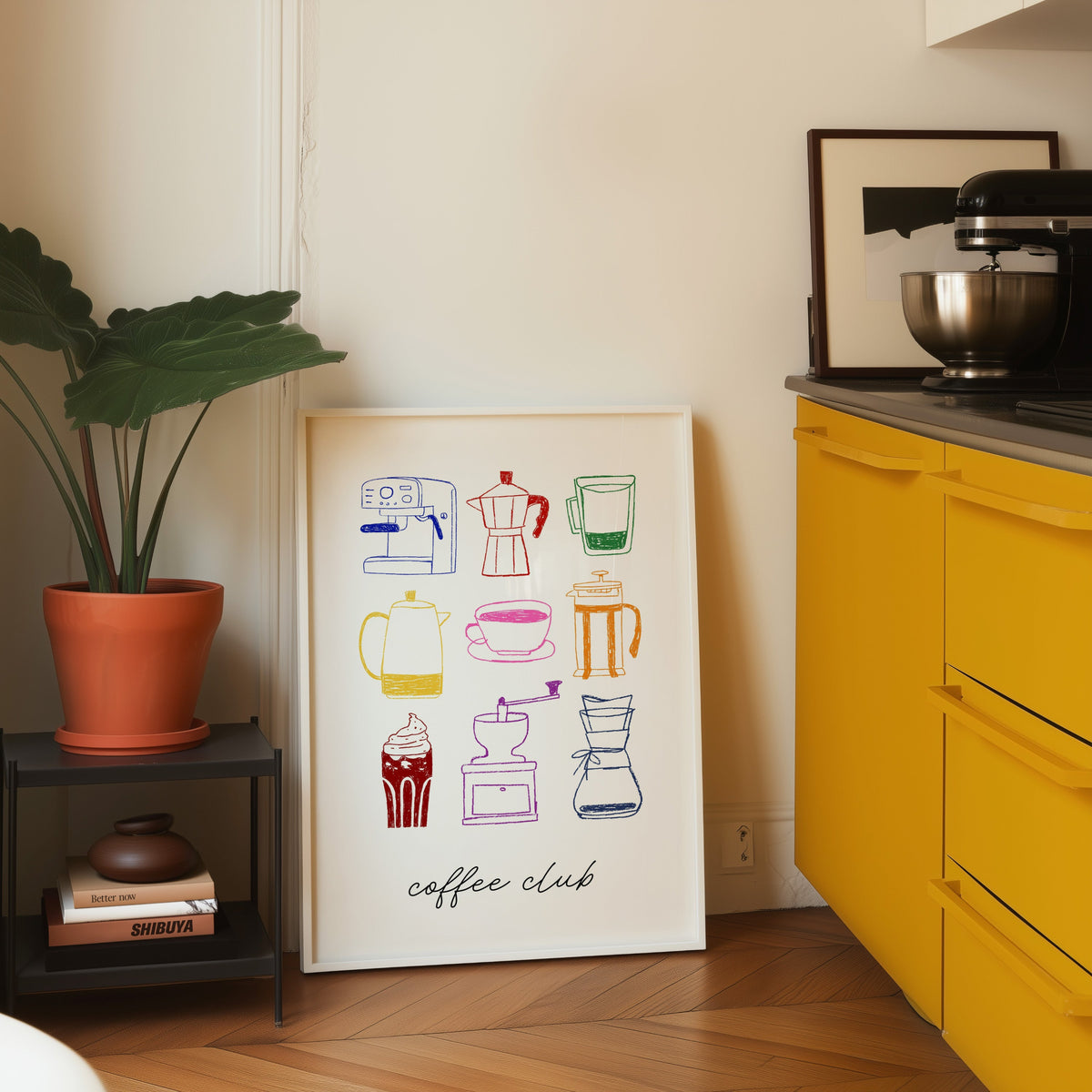 Coffee club print in a white frame leaning on parquet beside a bright yellow kitchen