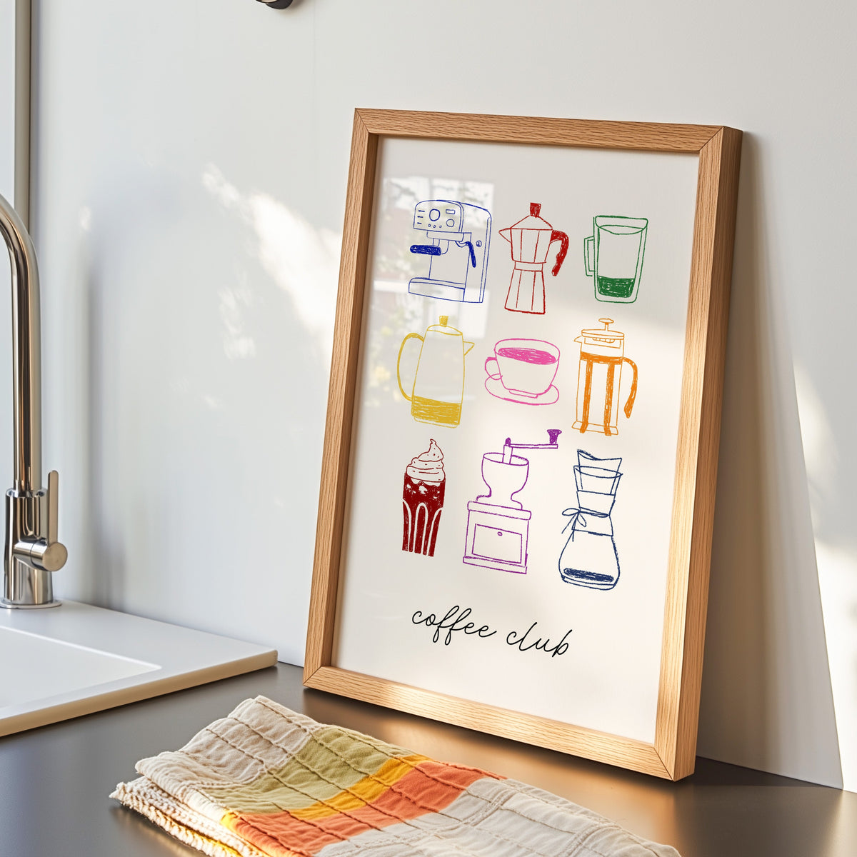 Coffee club print in an oak frame by the kitchen sink beside a striped tea towel
