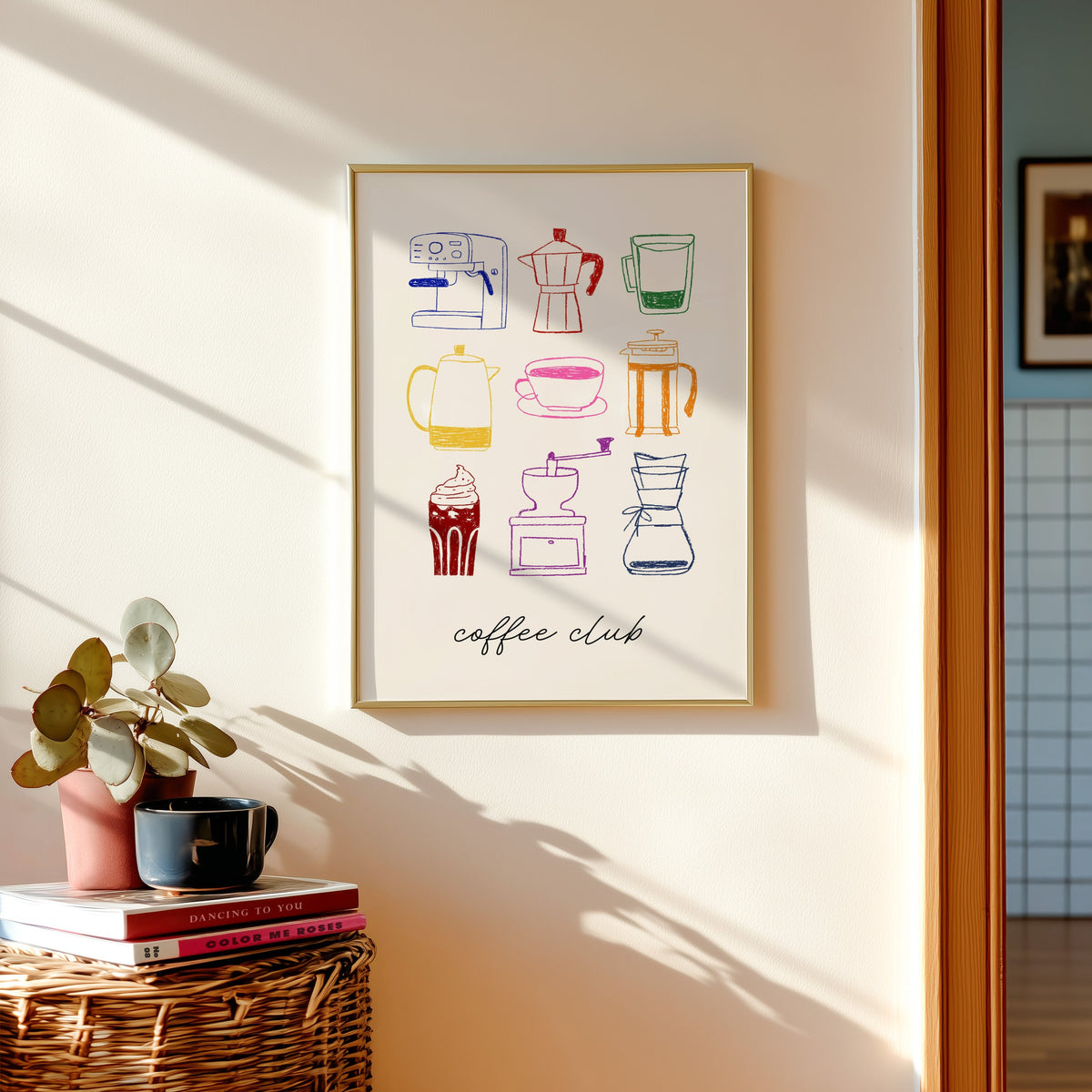 Coffee club print in a gold frame above a basket of books and a pilea plant