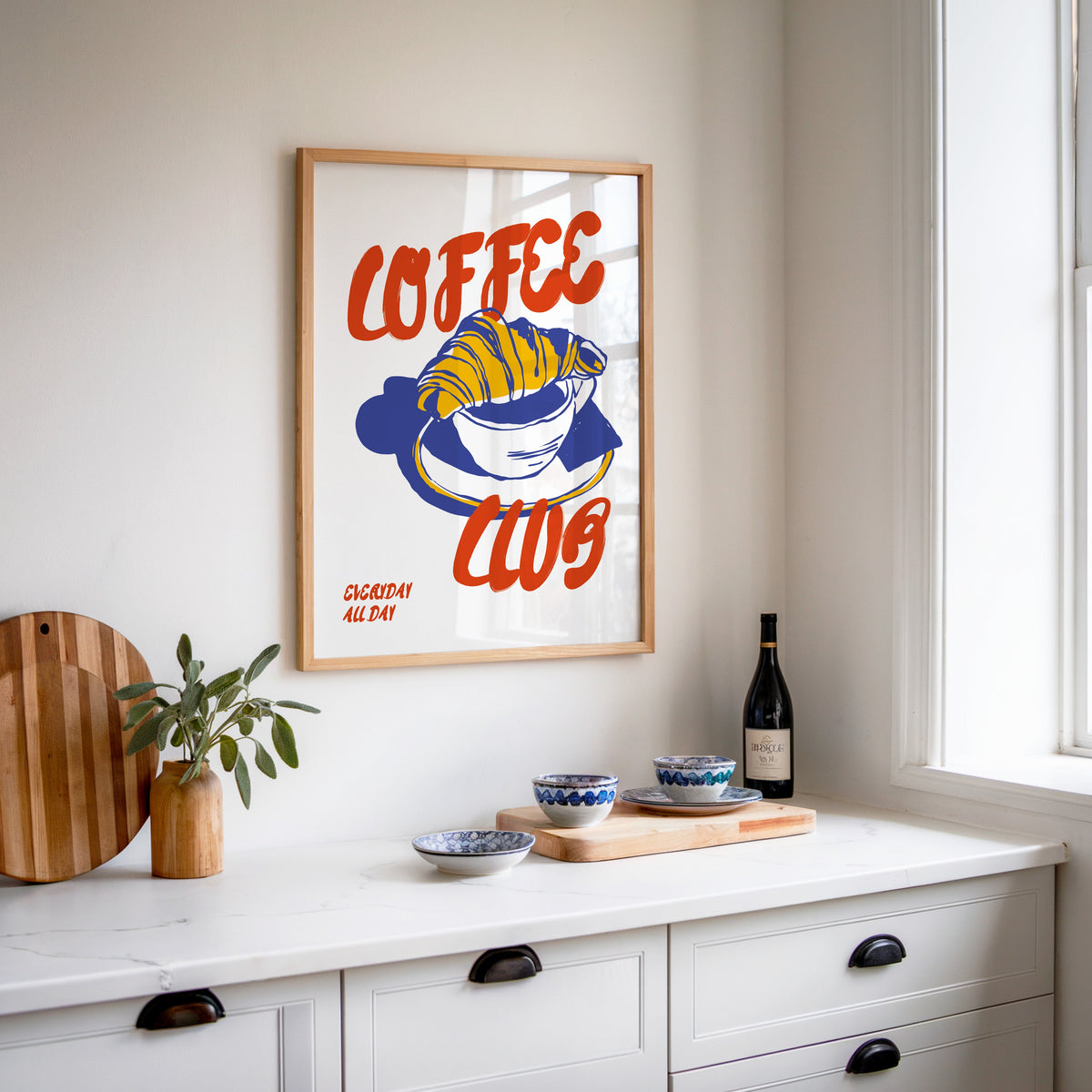 Coffee Club croissant print in an oak frame above a white kitchen sideboard