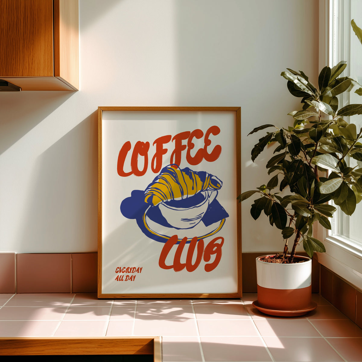 Coffee Club croissant print in an oak frame on pink tiles in afternoon sun