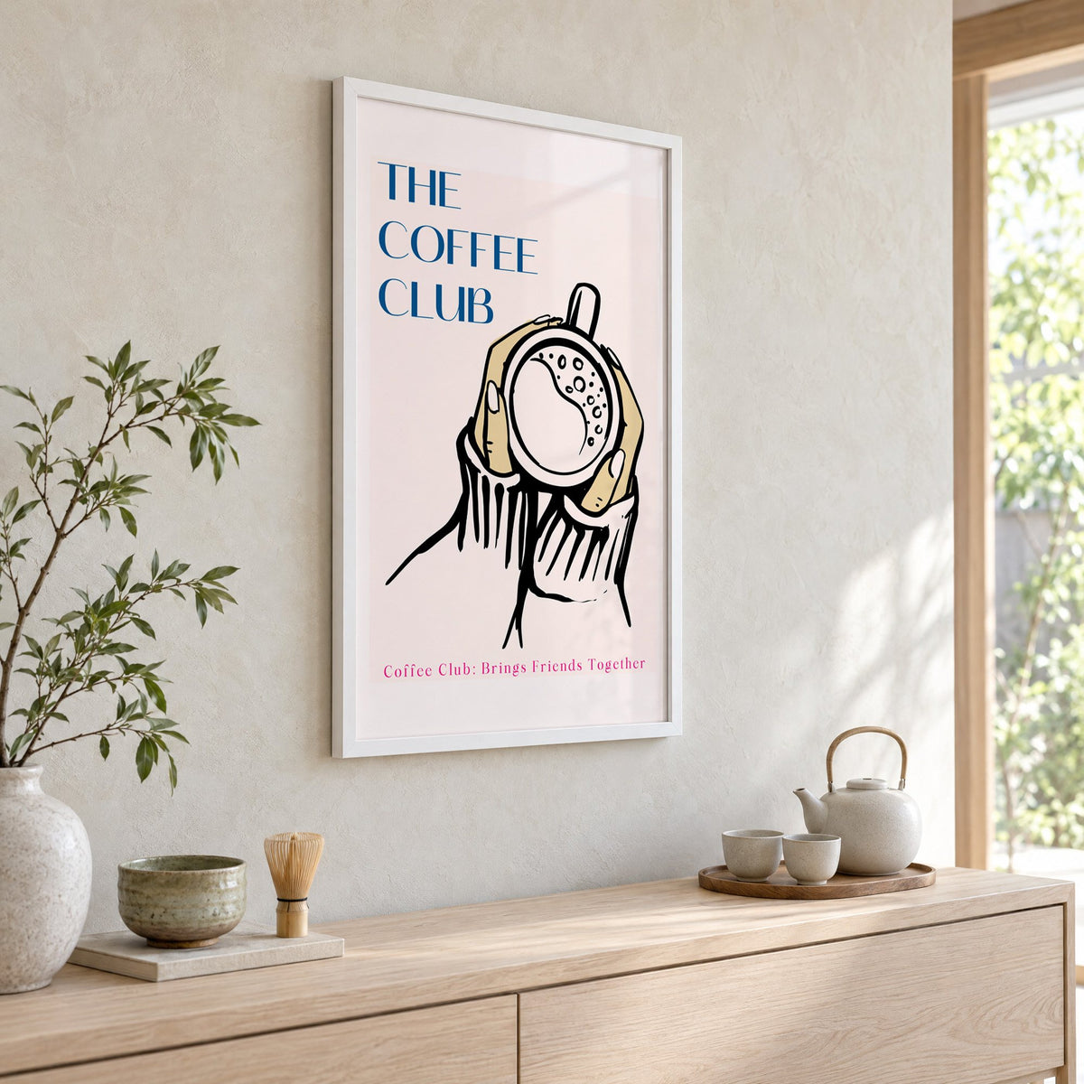 The Coffee Club hands and cup print in a white frame above a pale wood console with a matcha tea set