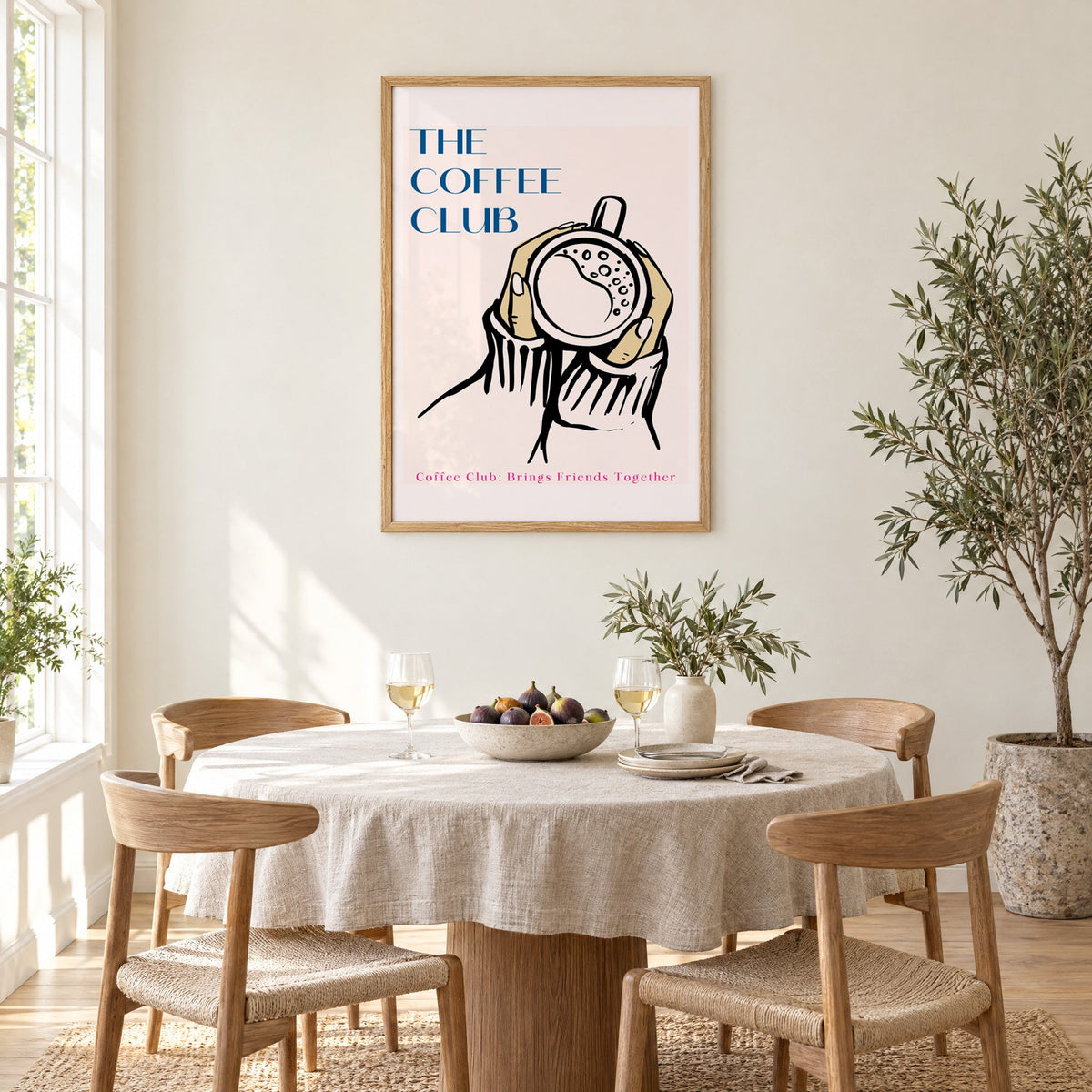 The Coffee Club hands and cup print in an oak frame above a round linen-covered dining table with figs and wine