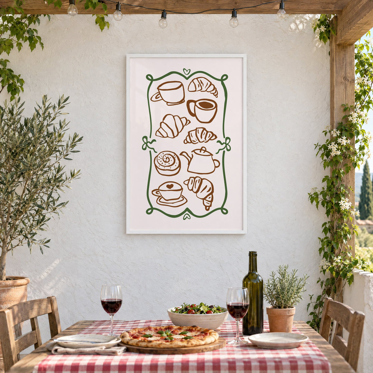 Coffee and croissant doodles green frame print in a white frame on a stucco wall above a checked-cloth table with pizza and red wine