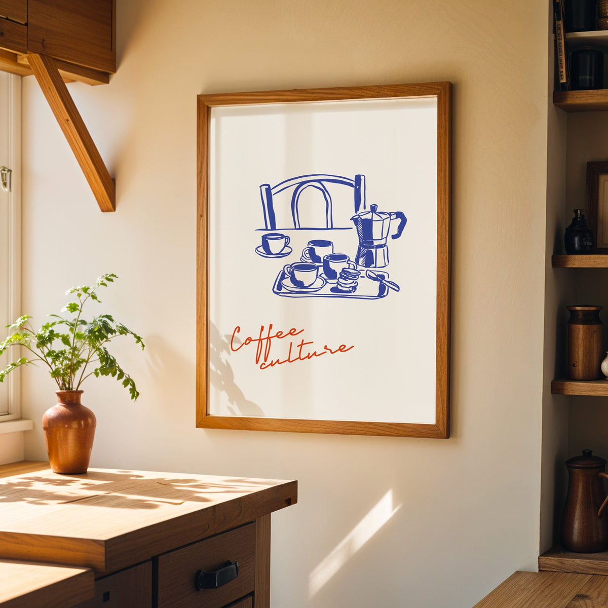 Blue ink moka pot print in a wood frame on a sunlit kitchen wall beside open shelving