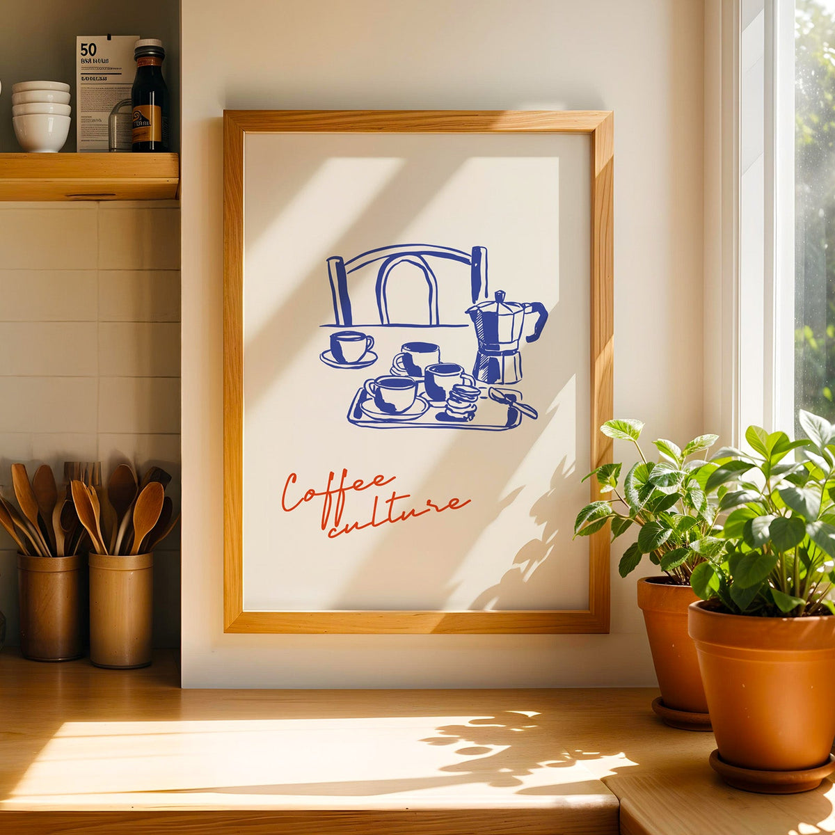 Moka pot print in a light wood frame on a butcher block counter by crocks of wooden utensils