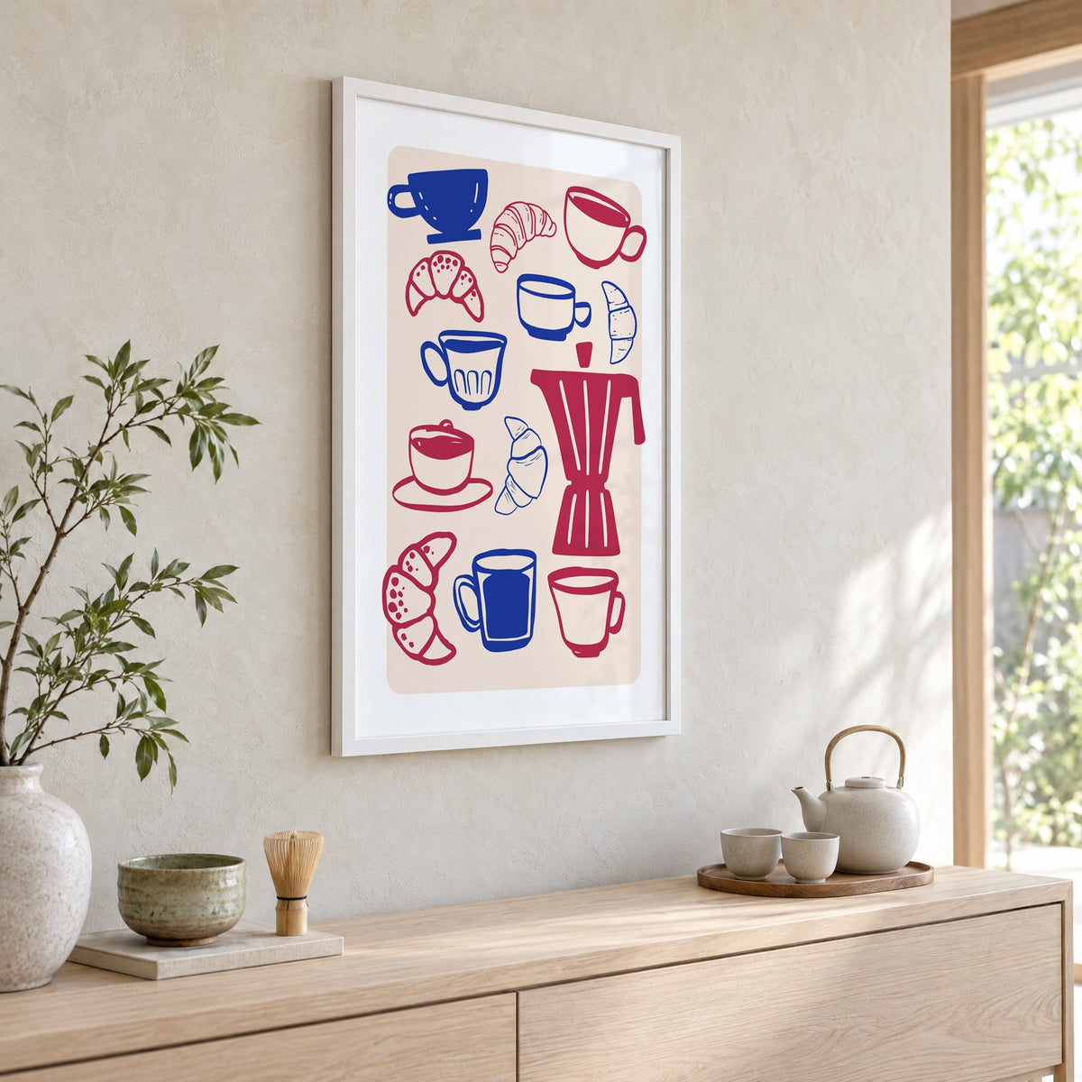 Moka pot, cups and croissants pattern in a white frame above a pale wood console with a matcha tea set