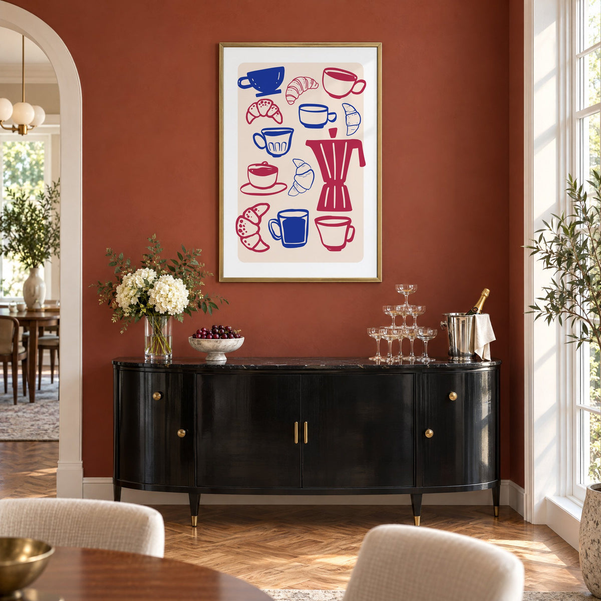 Moka pot, cups and croissants pattern in a brass frame on a terracotta wall above a black buffet with a champagne tower