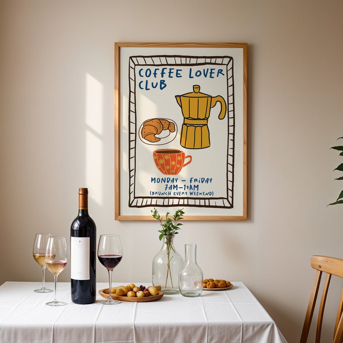 Coffee lover club moka pot print in an oak frame above a table laid with red wine and glasses