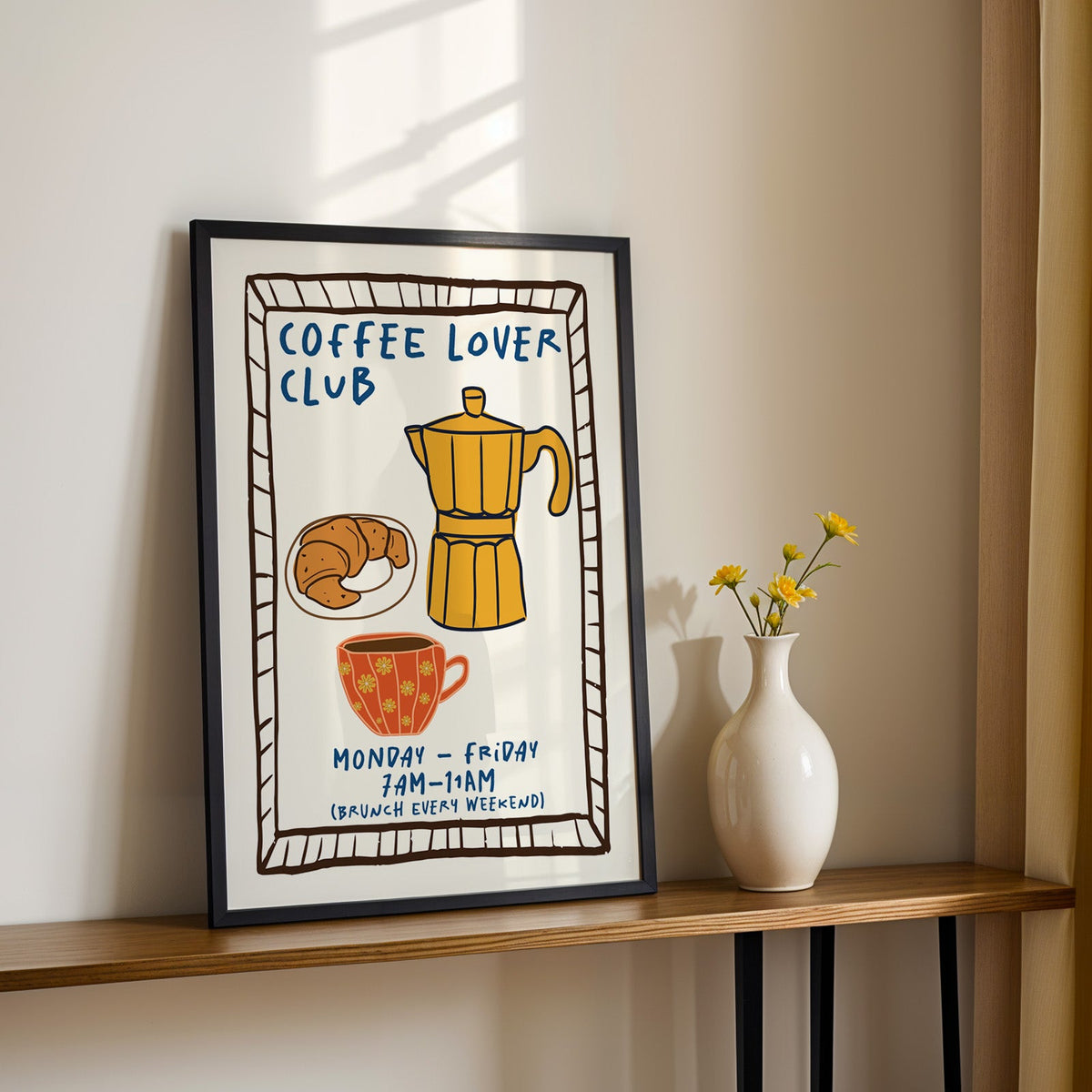 Coffee lover club moka pot print in a black frame on a console table with yellow daisies