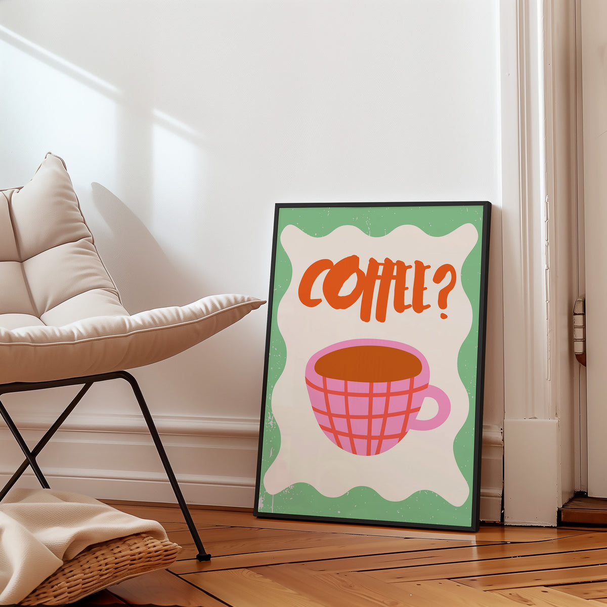 Pink check coffee cup print in a slim black frame leaning on a herringbone floor beside a cream armchair