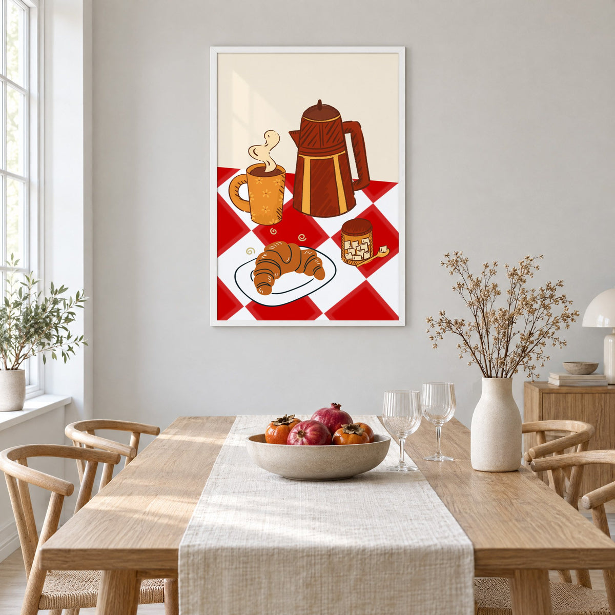 Coffee pot croissant red gingham print in a white frame above a light oak dining table with a linen runner and fruit bowl