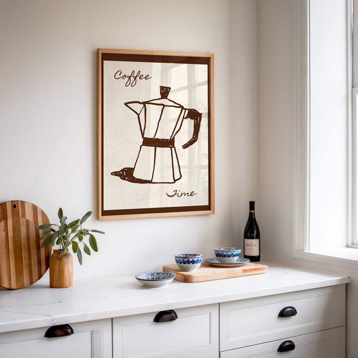 Coffee Time moka pot print in an oak frame above a white sideboard with a bottle of wine