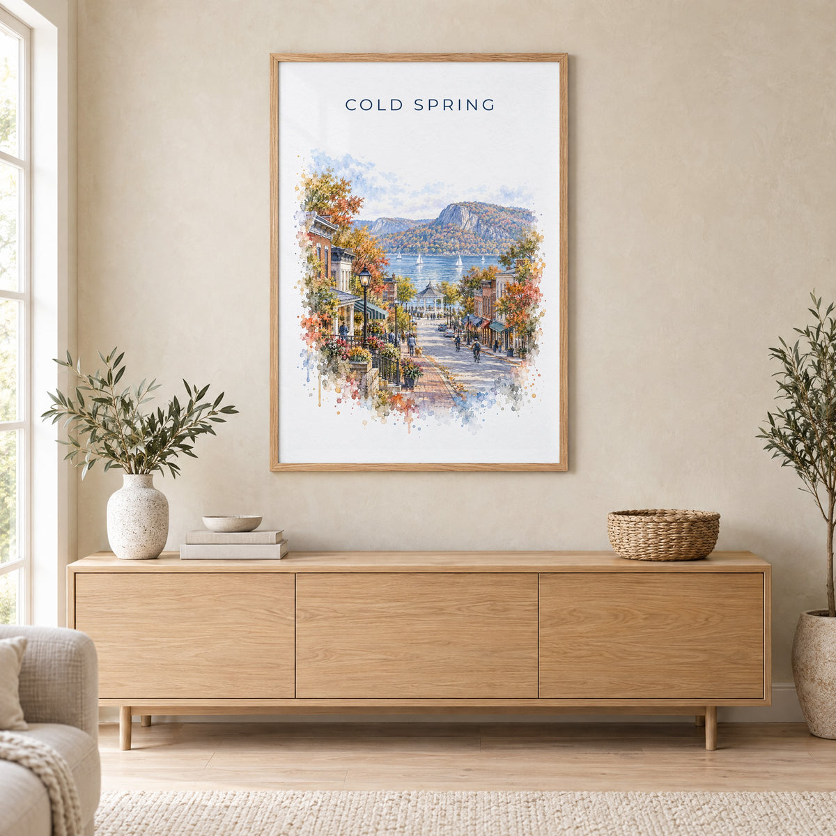 Cold Spring, New York watercolor print in an oak frame above a light wood sideboard in a Scandinavian living room