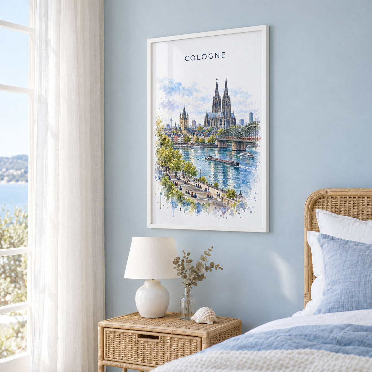 Cologne watercolor print in a white frame on a pale blue wall beside a rattan bed in a coastal bedroom