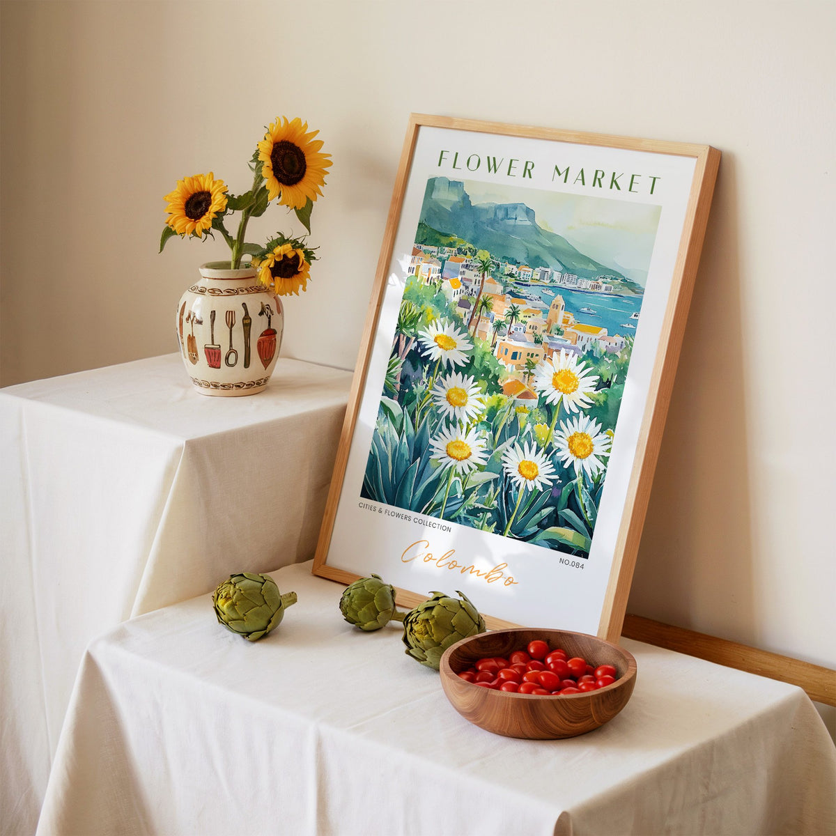 Colombo flower market print in an oak frame leaning on a linen-draped table beside a vase of sunflowers