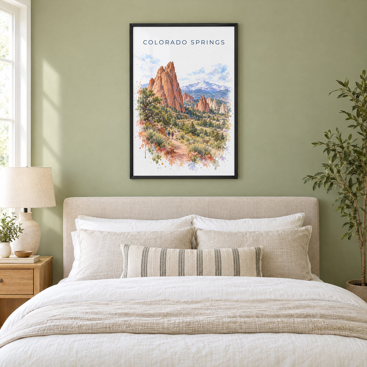 Colorado Springs watercolor print in a black frame above an upholstered headboard in a sage green bedroom