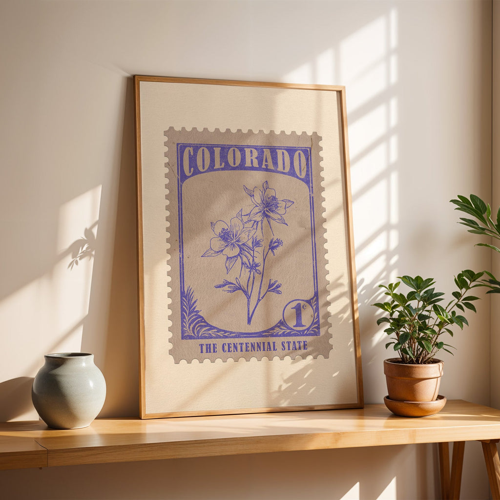 Colorado rocky mountain columbine stamp print in a light oak frame leaning on a wooden table beside a stoneware vase