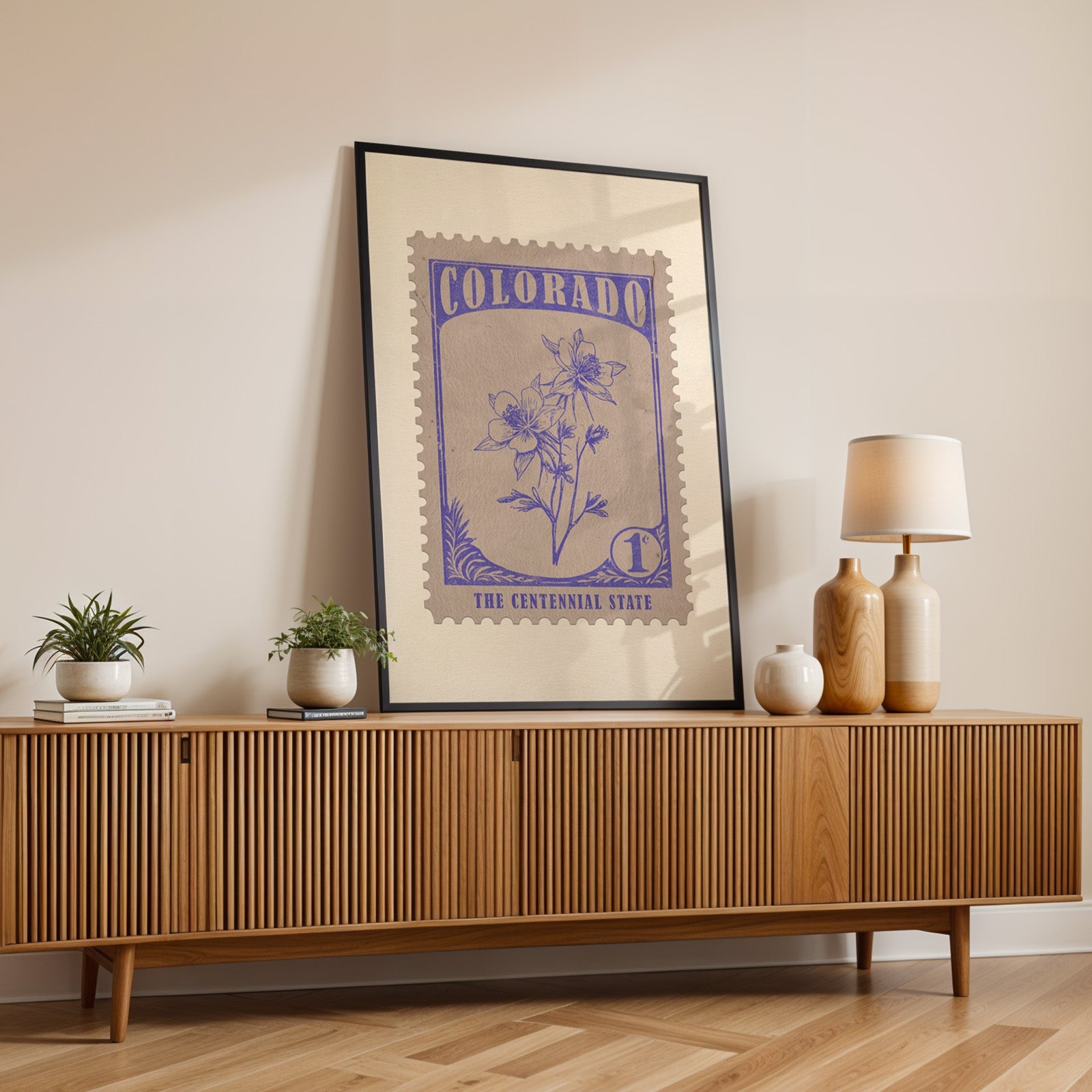 Colorado state flower print in a black frame leaning on a fluted wood credenza with vases and a lamp