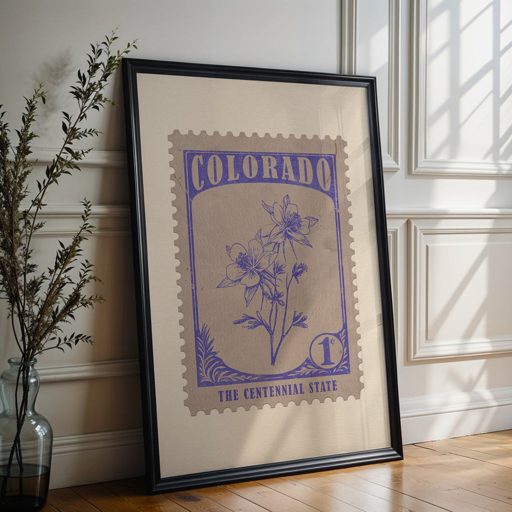 Colorado state flower print in a black frame leaning against a white panelled wall beside olive branches