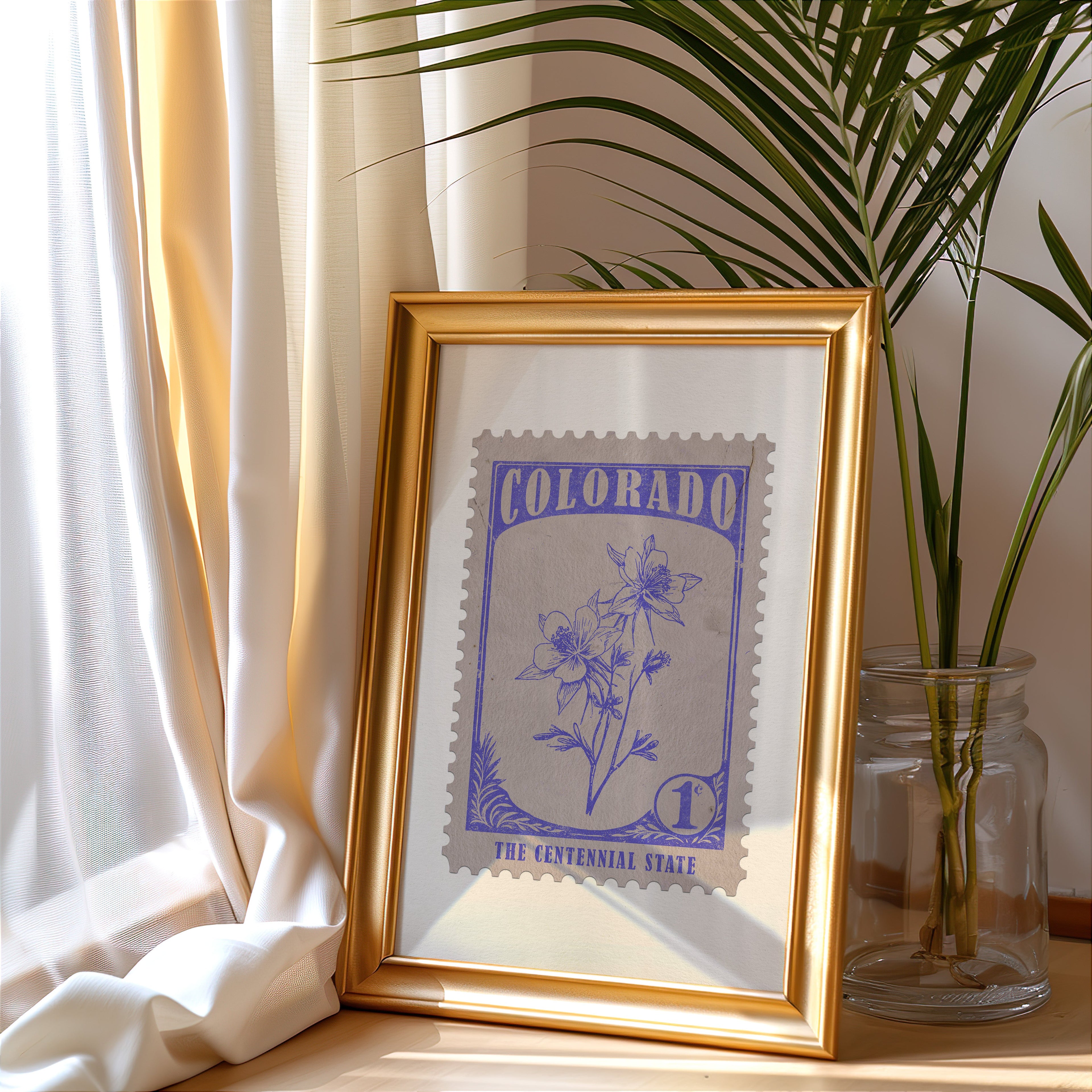 Colorado stamp print in a gold frame leaning by a cream curtain with a palm in a glass jar