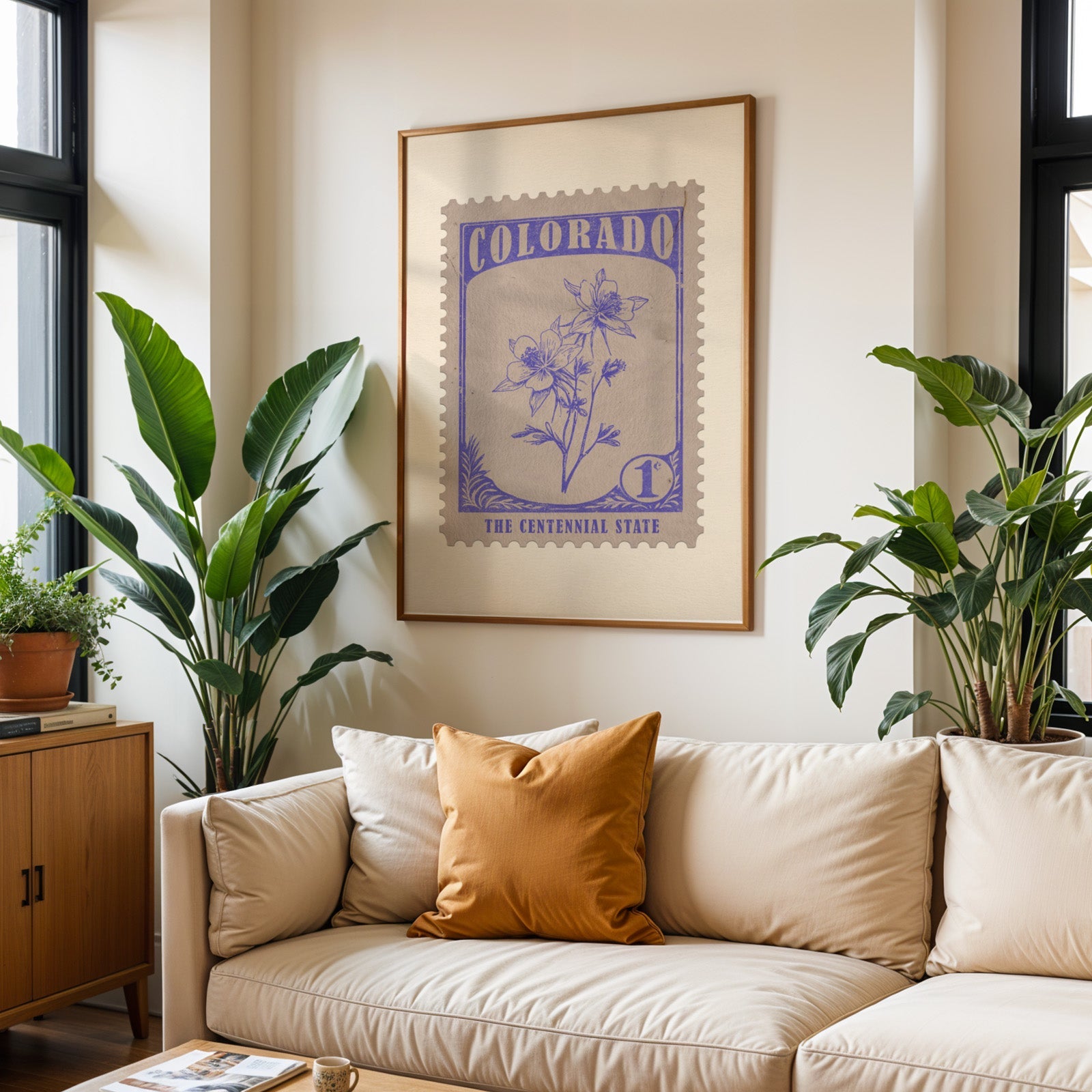 Colorado state flower print framed above a cream sofa with an ochre cushion and large plants either side