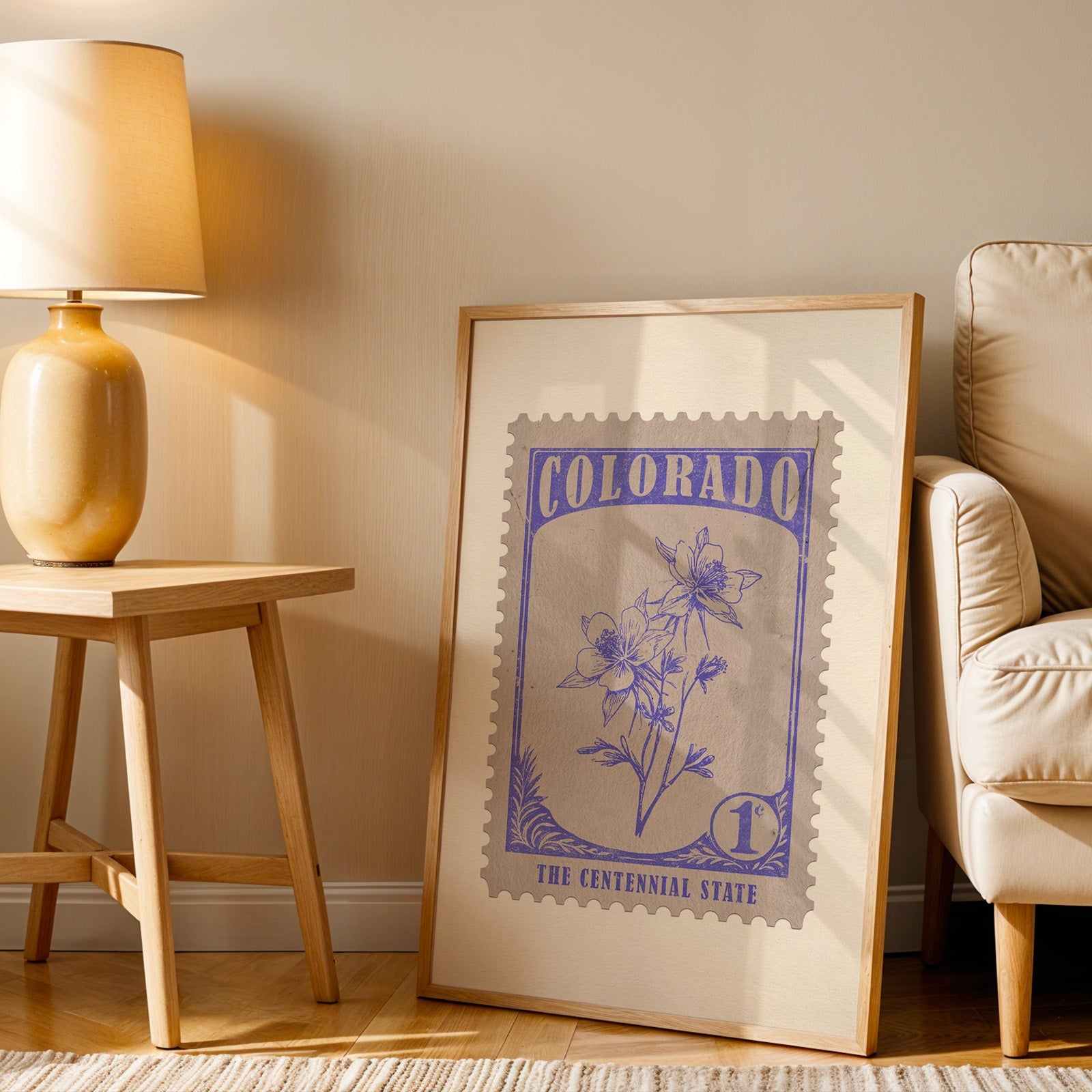 Colorado stamp print in a wood frame resting on the floor beside a beige armchair and a yellow lamp