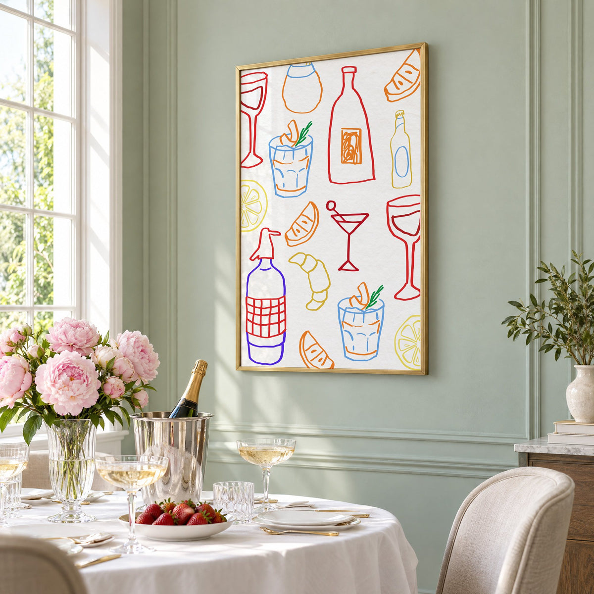 Colorful bar drinks doodle pattern print in a brass frame on a sage wall above a brunch table with champagne and peonies, seen at an angle