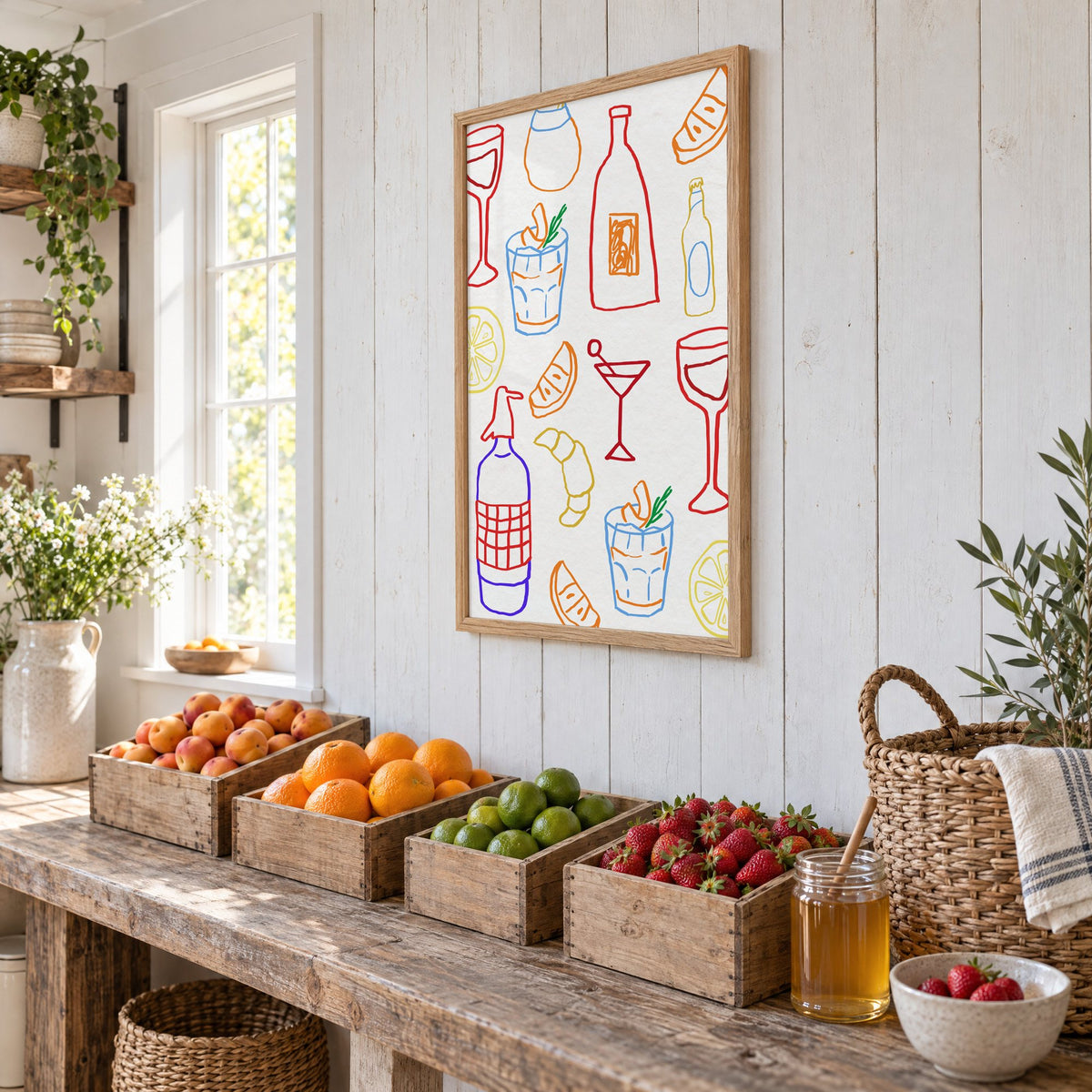 Colorful bar drinks doodle pattern print in an oak frame on white plank walls above wooden crates of fresh fruit, seen at an angle