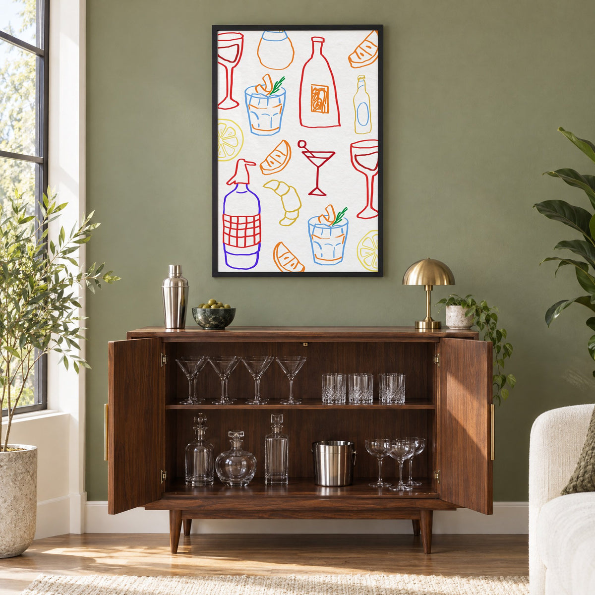Colorful bar drinks doodle pattern print in a black frame on an olive green wall above a walnut bar cabinet with glassware