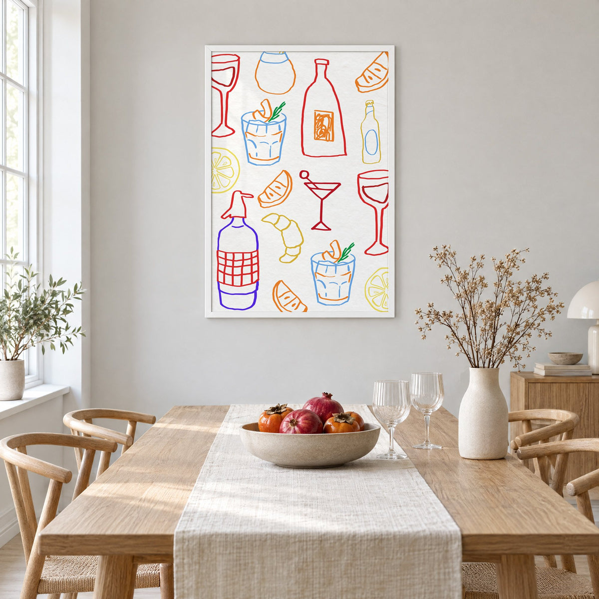Colorful bar drinks doodle pattern print in a white frame above a light oak dining table with a linen runner and fruit bowl